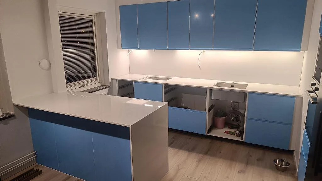 Køkkenbordplade i Crystal Diamond, poleret komposit, med køkkenø, väggbänk og rostfri vask i ett køkken under montering i Malmö.