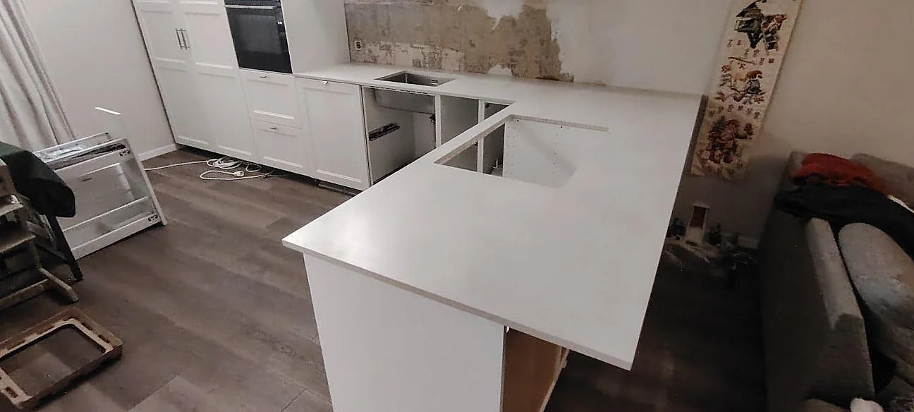 Mat køkkenbordplade i Dekton Albarium, lys keramik, på halvö og väggbänk med öppningar under montering i Gävle.