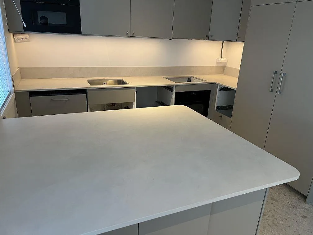 Mat køkkenbordplade i lys Dekton Albarium keramik med stor arbetsyta, låg stänkkant og diskbänkssida i ett køkken i Vällingby.