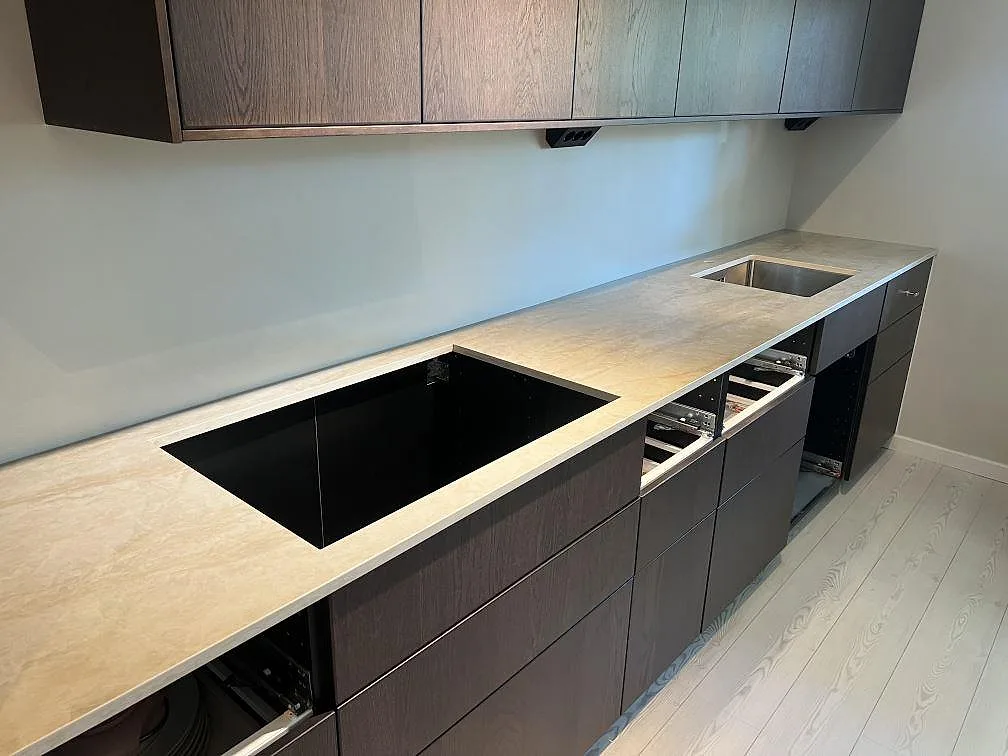 Lige køkkenbordplade i poleret Dekton Arga keramik, 20 mm, med kogeplade og vask under montering i ett køkken i Älvsjö.