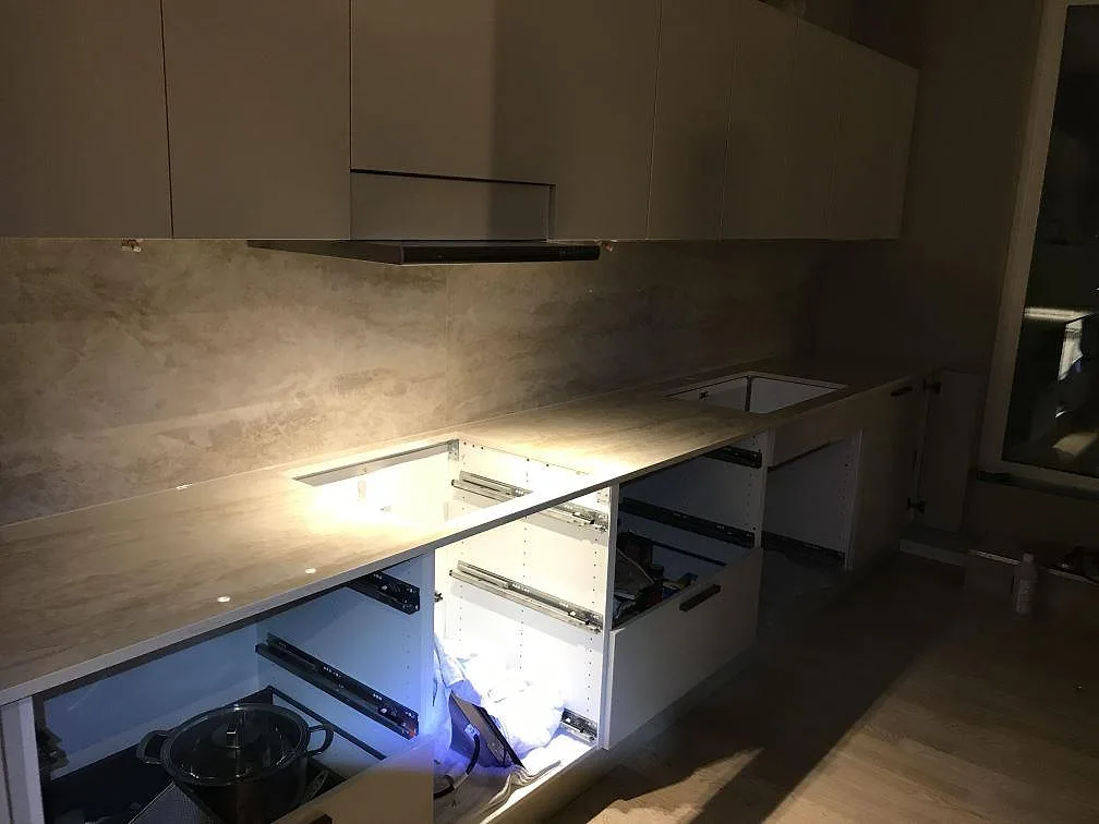 Køkkenbordplade og uppvikt stænkplade i ljusgrå marmorlik Dekton Arga i ett L-format køkken under montering