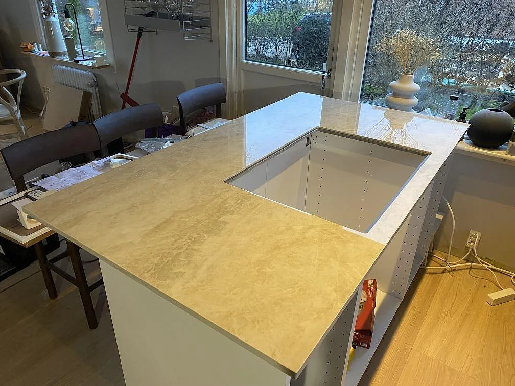 Køkkenø med 20 mm poleret Dekton Arga, lys keramik med beigegrå åretegning og en stor rektangulär öppning i ett køkken i Färlöv.