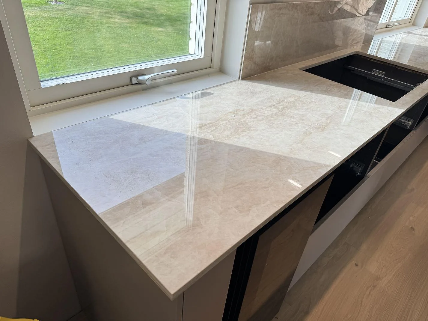 Køkkenbordplade i poleret Dekton Arga, lys beige keramik, med vindue, stænkplade og öppet udskæring i ett køkken i Gemla.