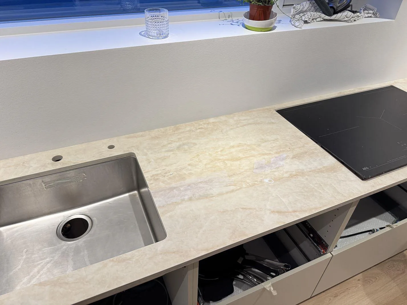 Køkkenbordplade i cremebeige Dekton Arga, 20 mm poleret, med infälld induktionshäll og underlimmad rostfri vask i en lang rad i ett køkken i Greve.