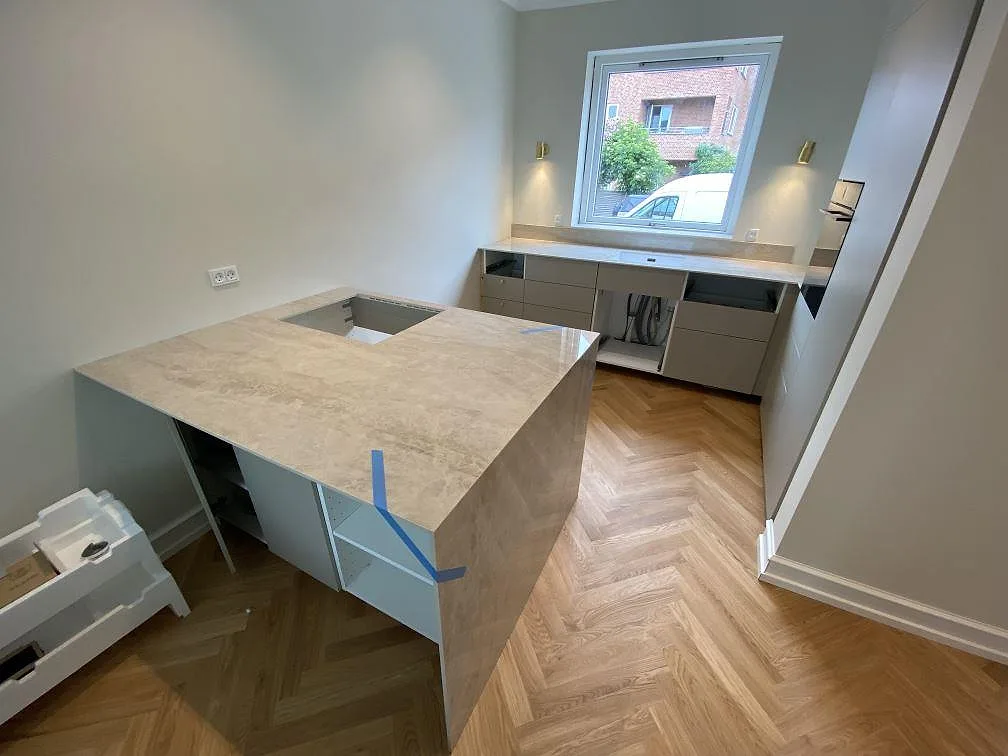 Køkkenbordplade i poleret Dekton Arga, 12 mm keramik, med fristående arbetsdel, vattenfallsida og lige diskbänk under vindue i Hellerup DK.