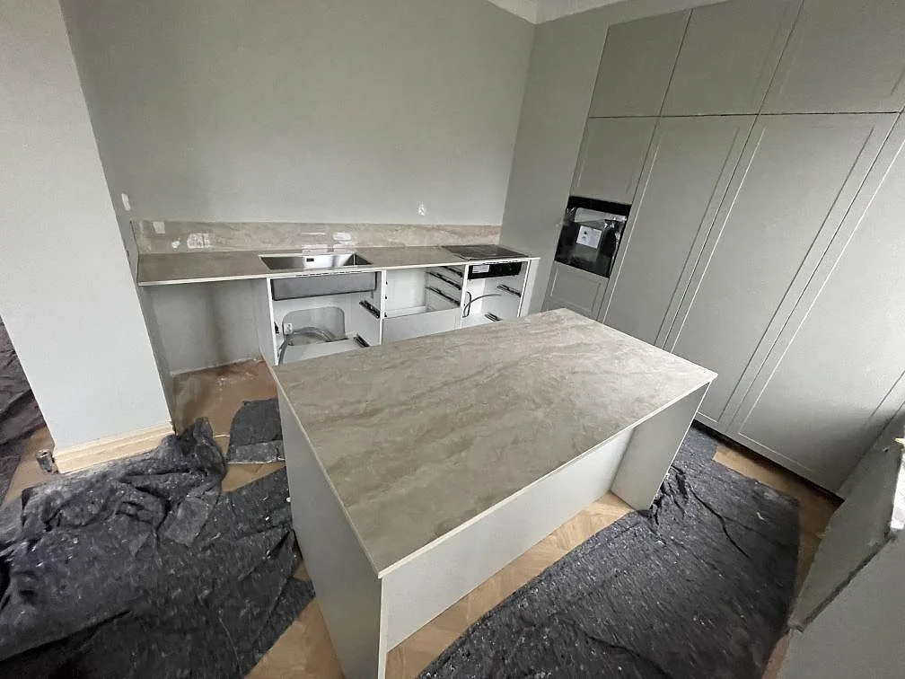 Køkkenbordplade og køkkenø i Dekton Arga, poleret lys marmorlik keramik, i ett U-format køkken under montering i Helsingborg.