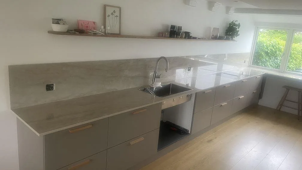 Køkkenbordplade i poleret Dekton Arga keramik med rostfri vask, kogeplade og matchande stænkplade i ett køkken i Holte.