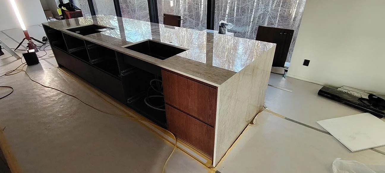 Poleret køkkenbordplade og køkkenø i lys beige Dekton Arga, keramik, med kogeplade og fallande sida i ett køkken i Huddinge.