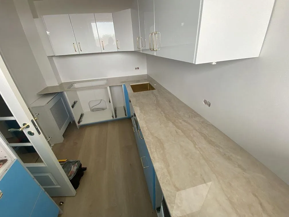 Køkkenbordplade i beige Dekton Arga, 20 mm poleret keramik, i ett kompakt køkken i Hvidovre med vask, hällurtag og öppna skabe under montering.