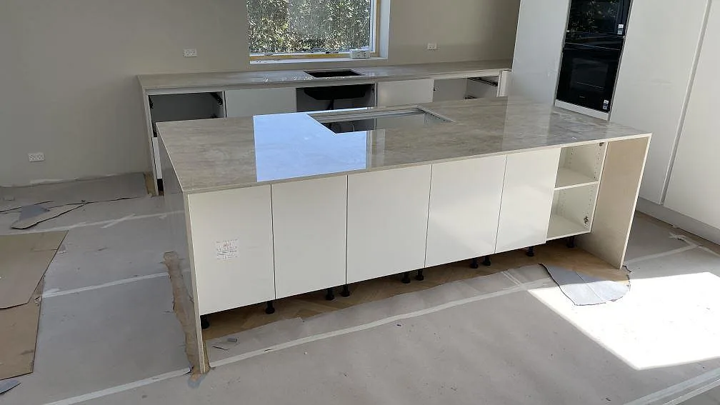 Køkkenbordplade i poleret Dekton Arga, keramik, med køkkenø og väggbänkar under montering i Ishöj.