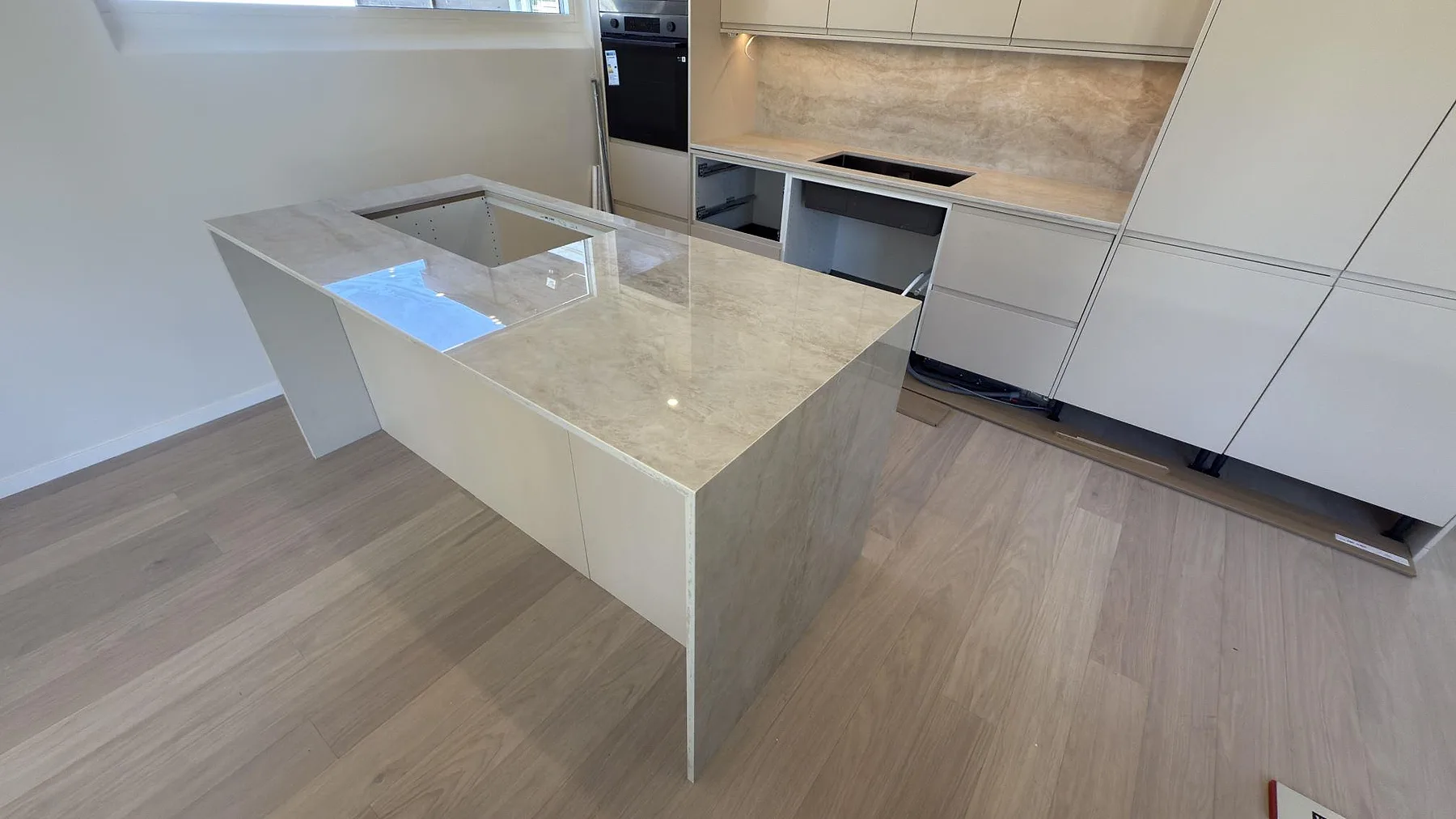 Køkkenbordplade i beige Dekton Arga, poleret keramik, på køkkenø i ett køkken i Järfälla med matchande stænkplade og plats for kogeplade.