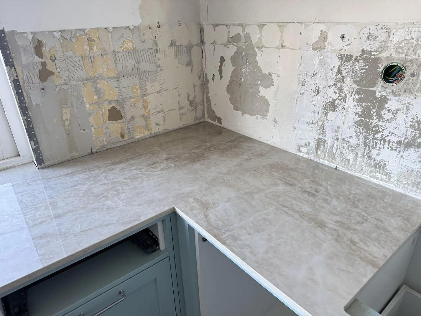 L-formad køkkenbordplade i poleret Dekton Arga, keramik, monteret på ljusblå köksstommar i Limhamn.