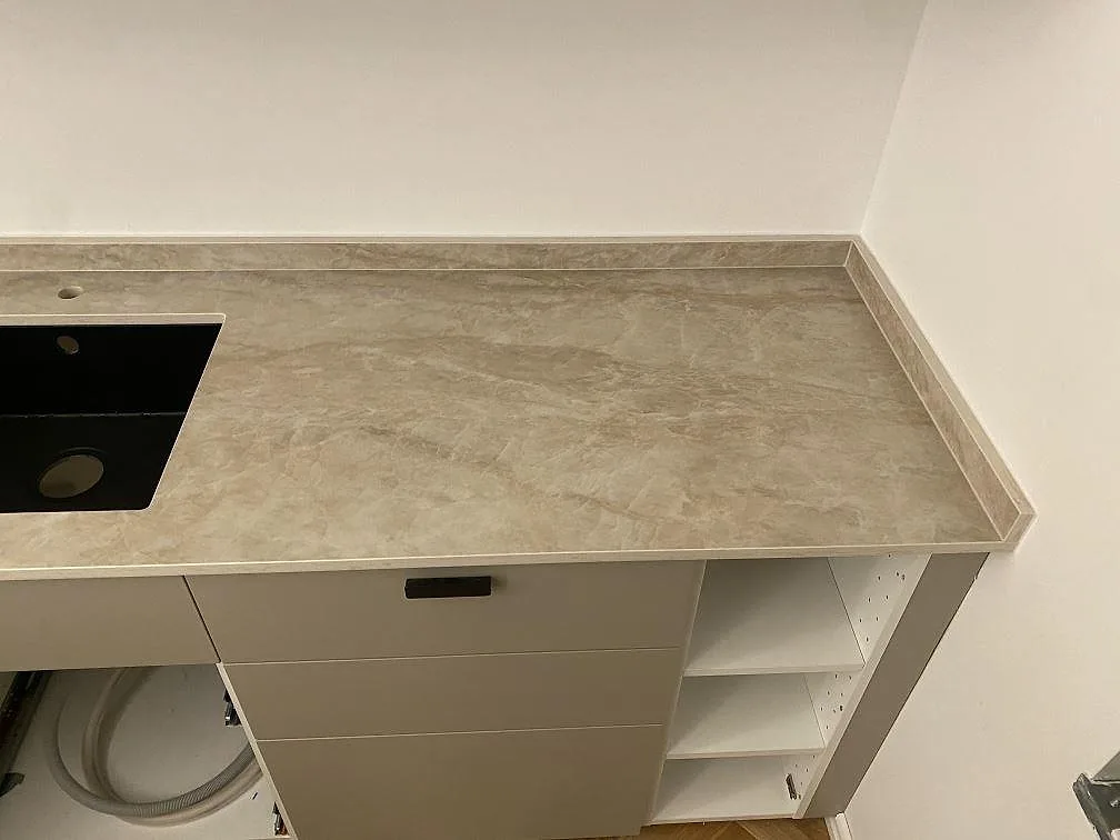 Køkkenbordplade i varmt gräddvit Dekton Arga keramik, poleret, med underlimmad sort vask og låga skabe i ett køkken i Malmö.