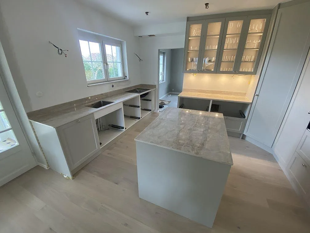 Køkkenbordplade og køkkenø i ljusgrå Dekton Arga, poleret, i ett køkken under montering i Malmö.