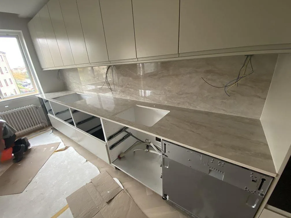 Køkkenbordplade i cremebeige Dekton Arga, poleret, med heltäckande stænkplade og underlimmad vask i ett køkken under montering i Mölndal.