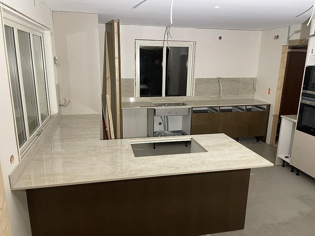 Poleret køkkenbordplade i keramik, Dekton Arga, med U-formad arbetsyta, peninsula og hällöppning i ett køkken under montering i Mora.