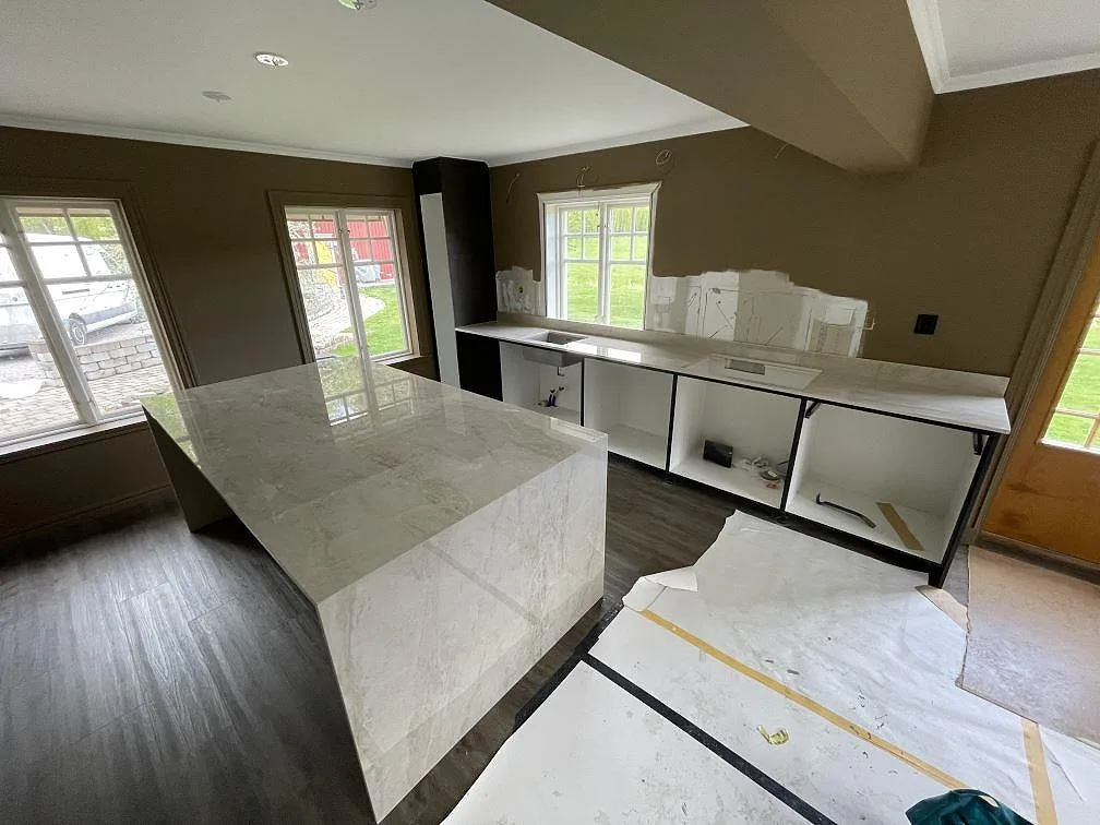 Køkkenbordplade og køkkenø i ljusgrå Dekton Arga, poleret keramik med marmorlik åretegning, monteret i ett køkken under installation i Sala.