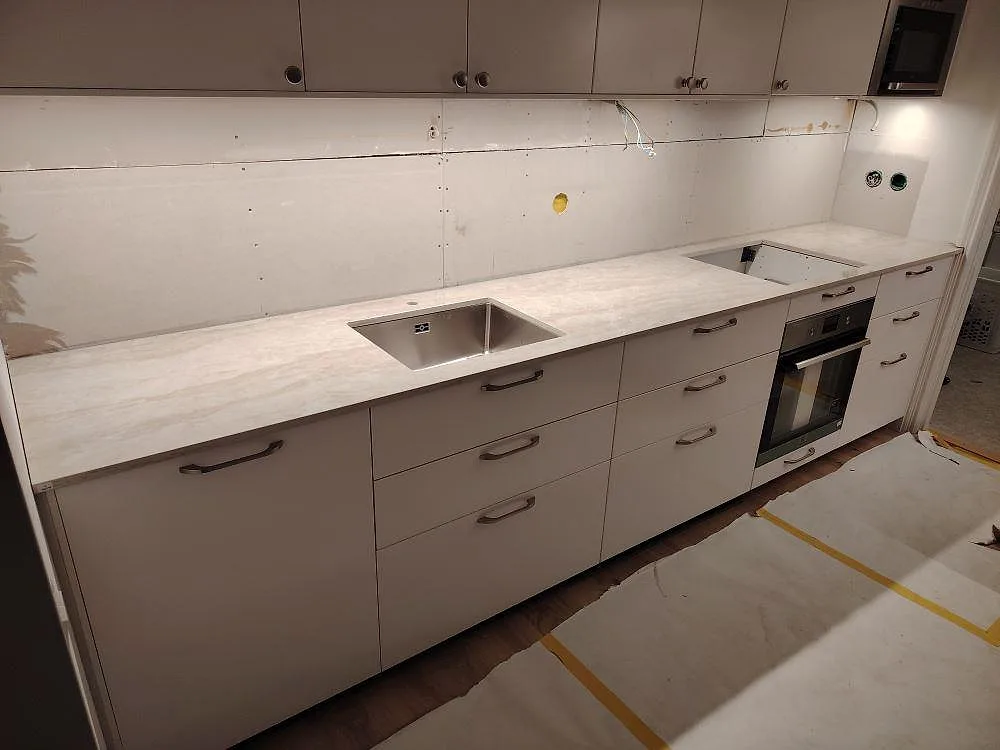 Køkkenbordplade i poleret Dekton Arga, 20 mm keramik, med vask og öppning for kogeplade i ett køkken under montering i Saltsjö Boo.