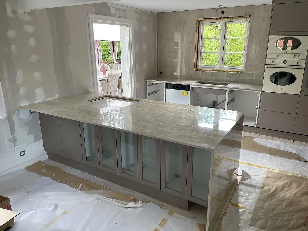 Poleret køkkenbordplade i Dekton Arga keramik med køkkenø, neddragen sidopanel, vask og vægbeklædning i ett køkken i Sandviken.