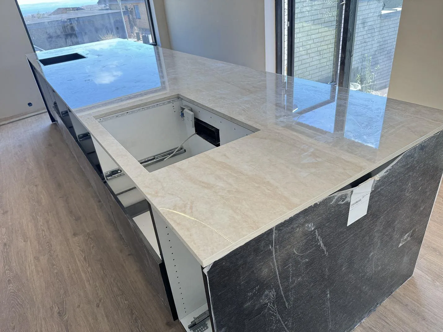 Køkkenbordplade i poleret Dekton Arga, keramik, med öppna köksstommar og udskæringer under montering i Skødstrup.