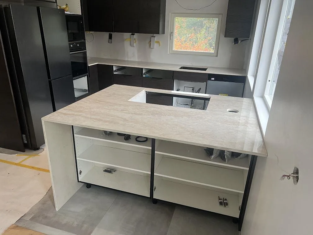 Poleret køkkenbordplade i Dekton Arga, lys keramik, med køkkenø og förberedda udskæring i ett køkken i Skogås under montering.