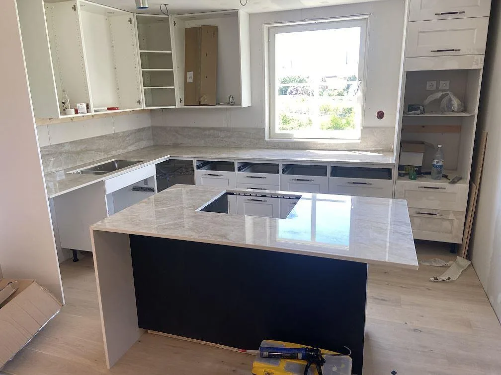 Køkkenbordplade og køkkenø i Dekton Arga, poleret krämvit keramik med brun-guldig åretegning, med underlimmad vask og infälld induktionshäll i ett køkken i Sölvesborg.