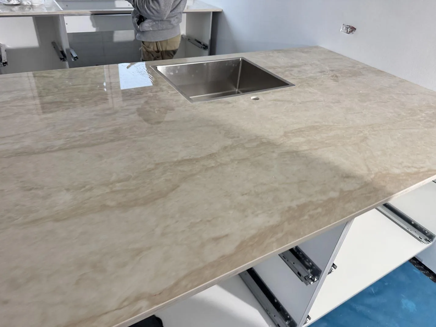 Køkkenbordplade i poleret krämbeige Dekton Arga keramik på en fristående køkkenø med centrerad underlimmad rostfri vask i ett køkken i Stenløse.