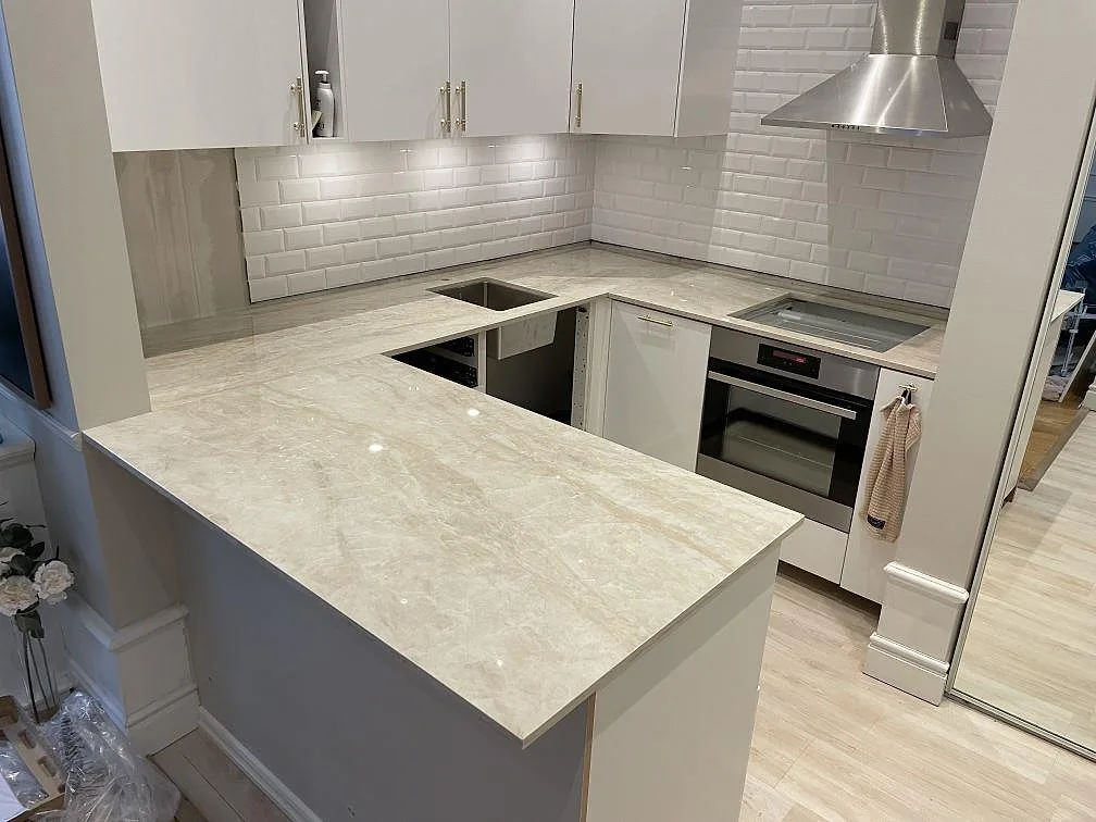 Køkkenbordplade i poleret Dekton Arga, lys keramik med marmorlik åretegning, i ett U-format køkken med halvö, diskhoöppning og hällplats i Stockholm.