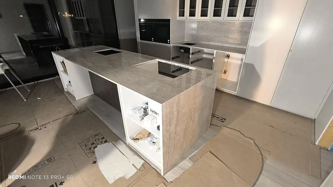 Køkkenø og køkkenbordplade i poleret Dekton Arga, keramik, med öppningar for vask og kogeplade i ett køkken under montering i Tranås.