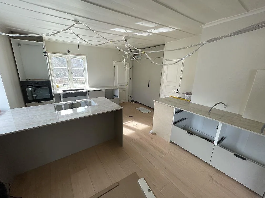 Køkkenbordplade i lys poleret Dekton Arga, keramik, med køkkenø og väggbänk under montering i Västerås.