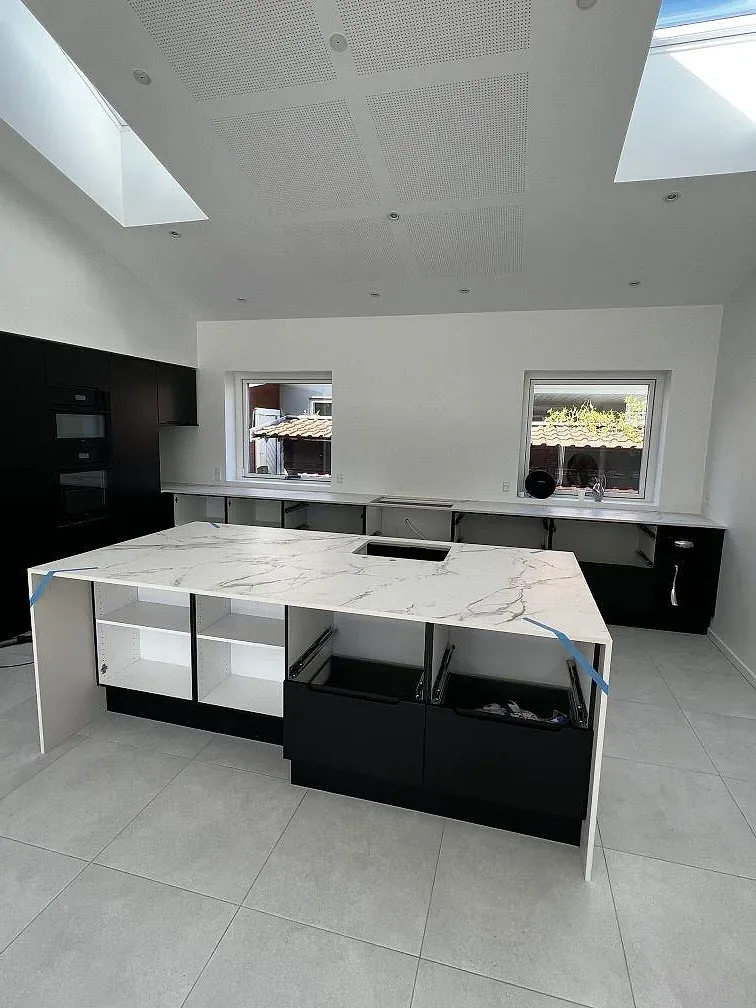 Køkkenø i hvid Dekton Aura 22 under montering, med mørke skabe og grått klinkergolv i ett køkken i Rødovre.