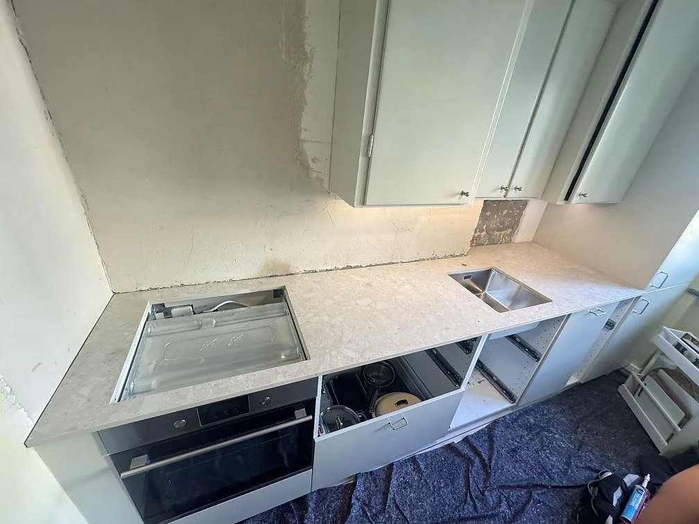 Køkkenbordplade i mat Dekton Ava, lys keramik med stenmönster, med hällzon og rostfri vask i ett køkken under montering i Malmö.