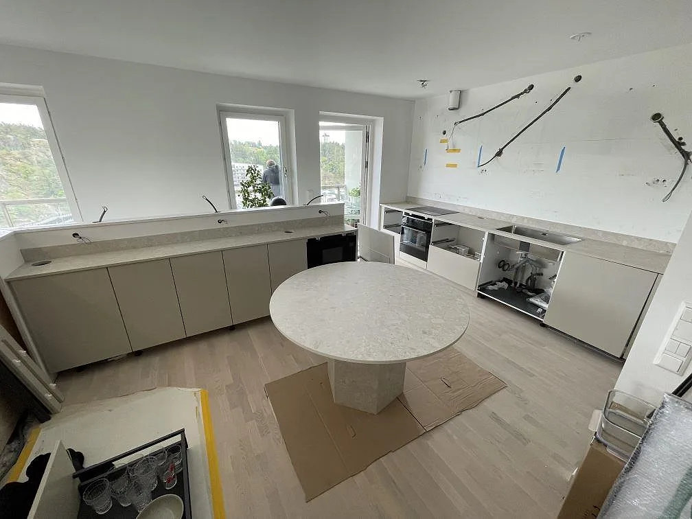Køkkenbordplade i mat Dekton Ava med lige väggbänk, rund central arbetsyta og stænkplade i ett køkken i Nacka.