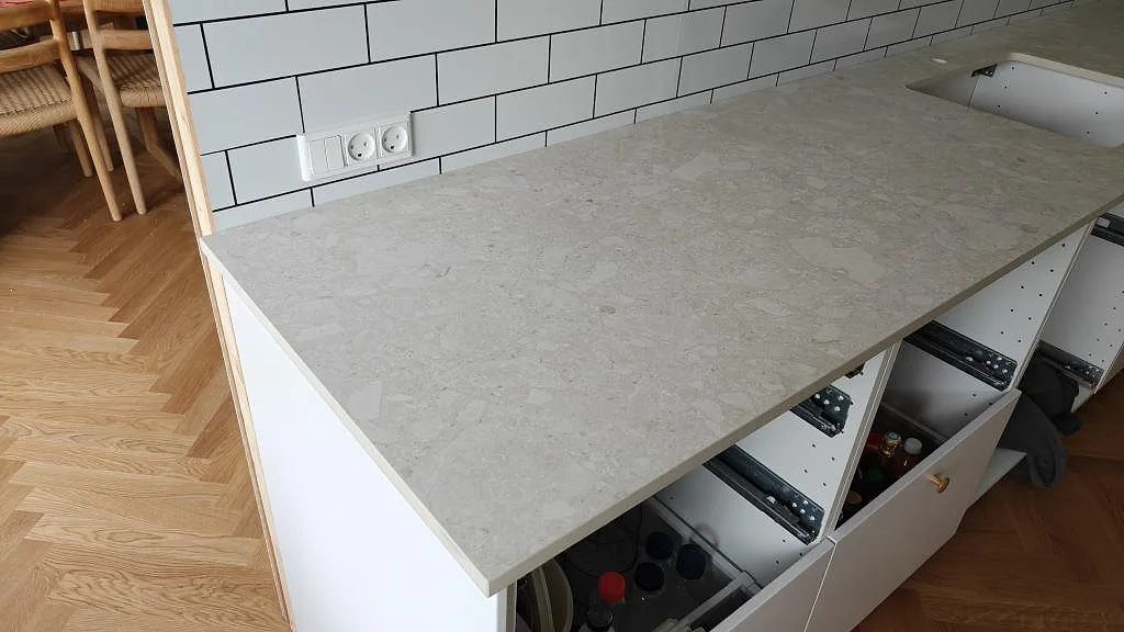 Køkkenbordplade i mat Dekton Ava keramik med lys stenbild, kaklad væg og öppen skåpstomme i ett køkken i Tåstrup.