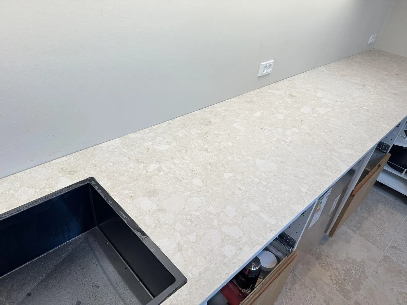 Køkkenbordplade i mat Dekton Ava, lys keramik, längs en væg med mørk vask og öppna skåpstommar i Værløse.