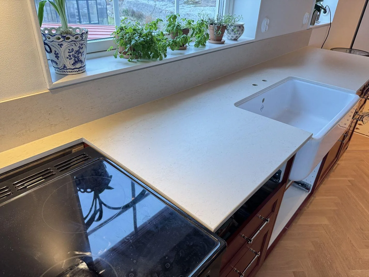 Køkkenbordplade i mat Dekton Danae keramik med hvid vask, sort kogeplade og uppvikt stænkplade i ett køkken i Hakenäset.