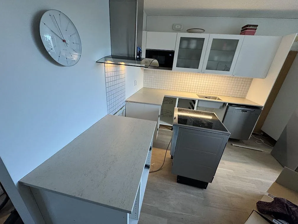 Køkken i Limhamn med Bordplader i 20 mm mat Dekton Danae under montering, med lyse väggplattor og öppna skabe.