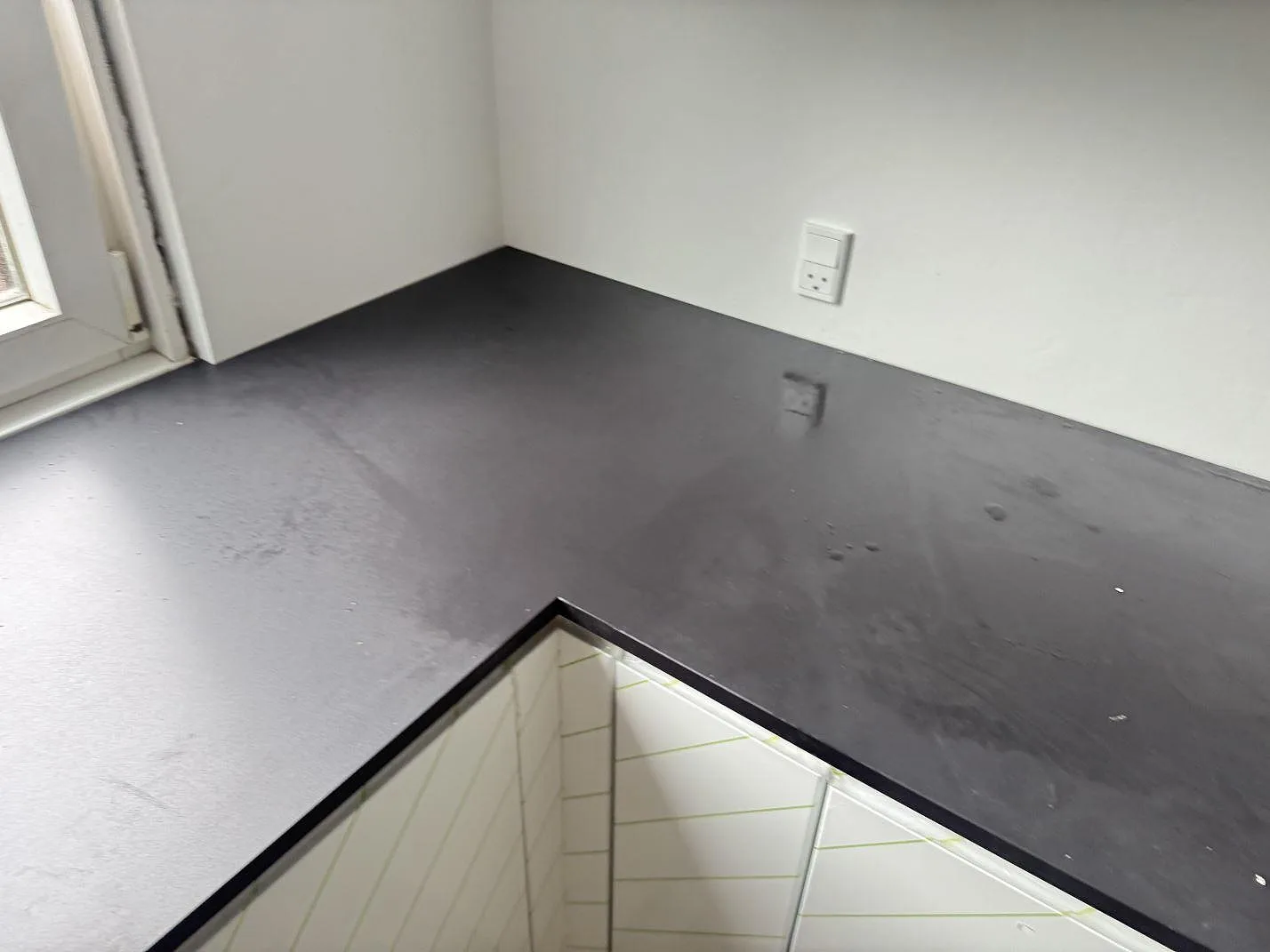 Køkkenbordplade i mørk mat Dekton Domoos, 20 mm, längs ett hjørner og vindue i ett køkken i Glostrup.