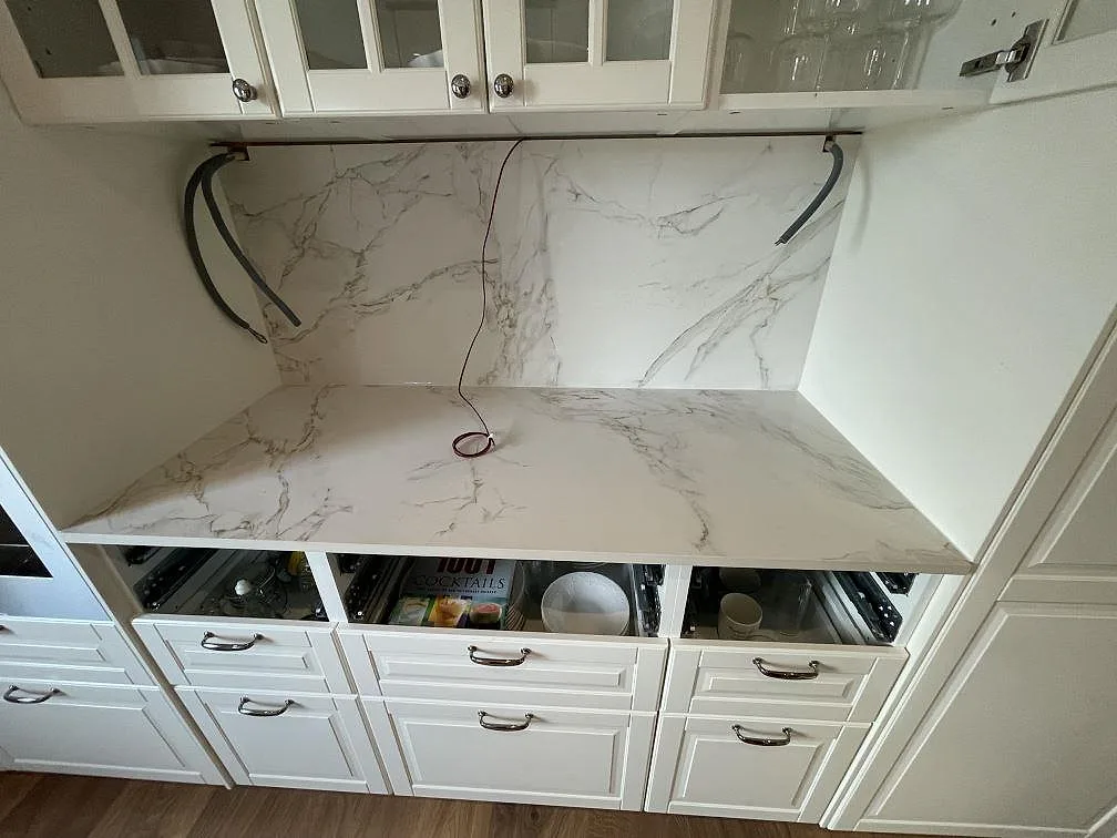 Køkkenbordplade og stænkplade i vitt Dekton Entzo med grå åretegning, mat overflade, i ett køkken under montering i Borlänge.