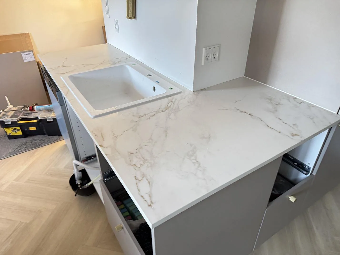 Køkkenbordplade i mat Dekton Entzo, hvid keramik med gråbeige åretegning, med vask og arbetsyta under montering i Danmark.
