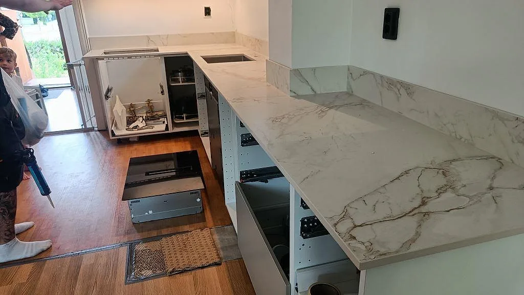 Køkkenbordplade i hvid Dekton Entzo med marmorlik åretegning, monteret i ett L-format køkken i Malmö under installationen med öppna skabe og rostfri vask.