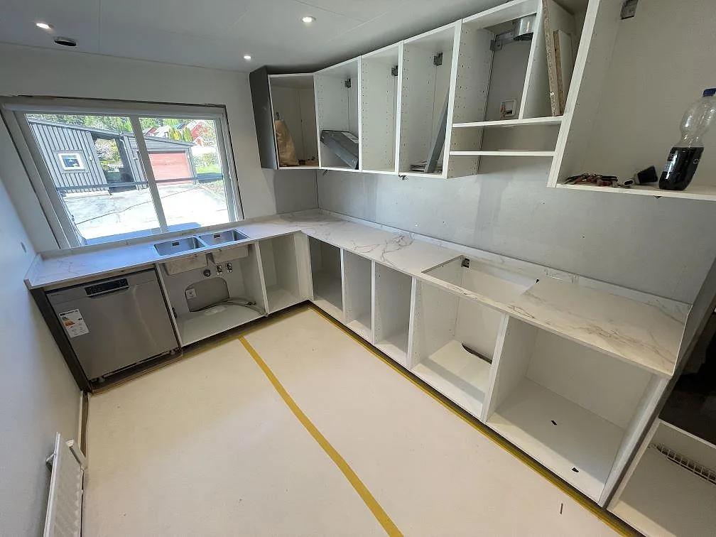 Køkkenbordplade i hvid Dekton Entzo, mat keramik med grå og gyllene åretegning, monteret over en L-formad köksdel under montering i ett køkken i Västerås.