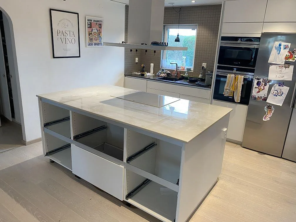 Køkkenbordplade i poleret Dekton Helena med køkkenø og kogeplade i ett ljust køkken i Trelleborg.