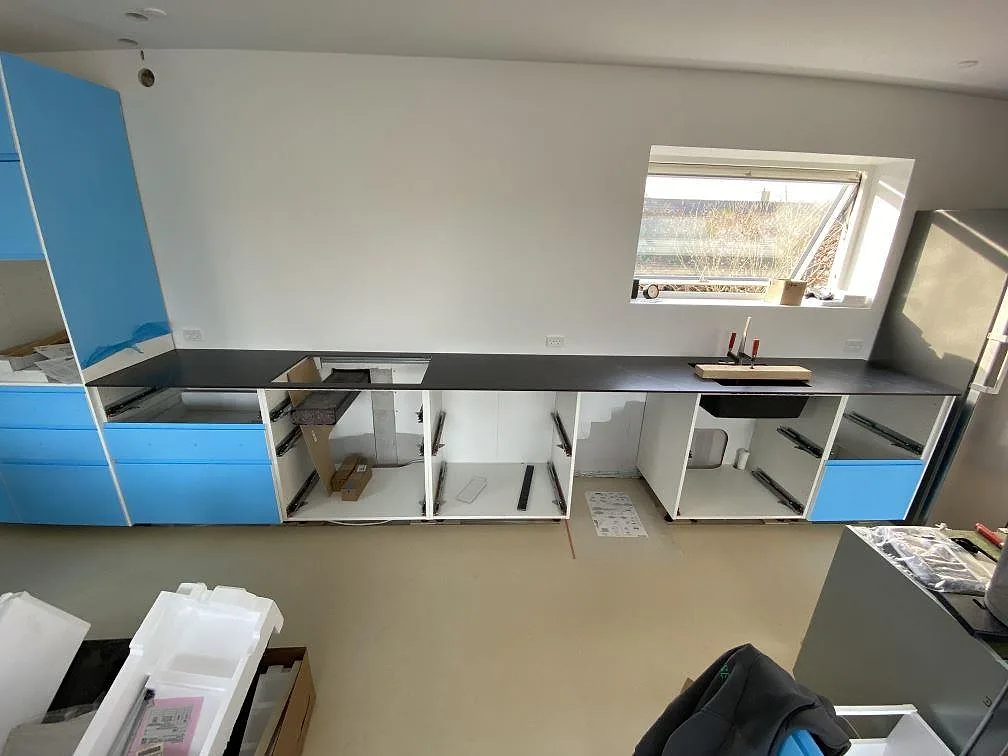 Køkkenbordplade i mat Dekton Kelya, mørk keramik, monteret längs blå köksstommar i Birkerød.