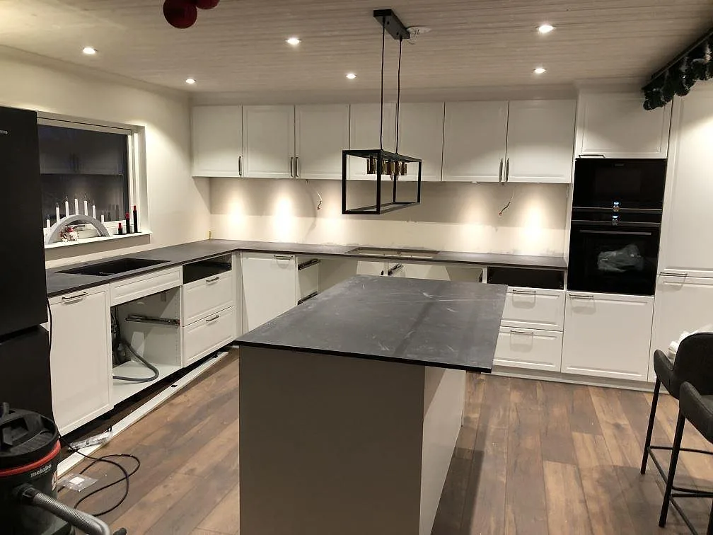 Køkkenbordplade og køkkenø i Dekton Kelya, mat mörkgrå keramik med lys åretegning, i ett køkken under montering i Kärna.