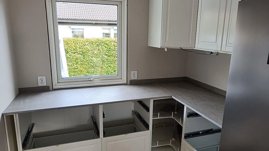 L-formad køkkenbordplade i mat Dekton Keon keramik, 20 mm, med grå overflade og stänkkant under fönstret i Anderstorp.