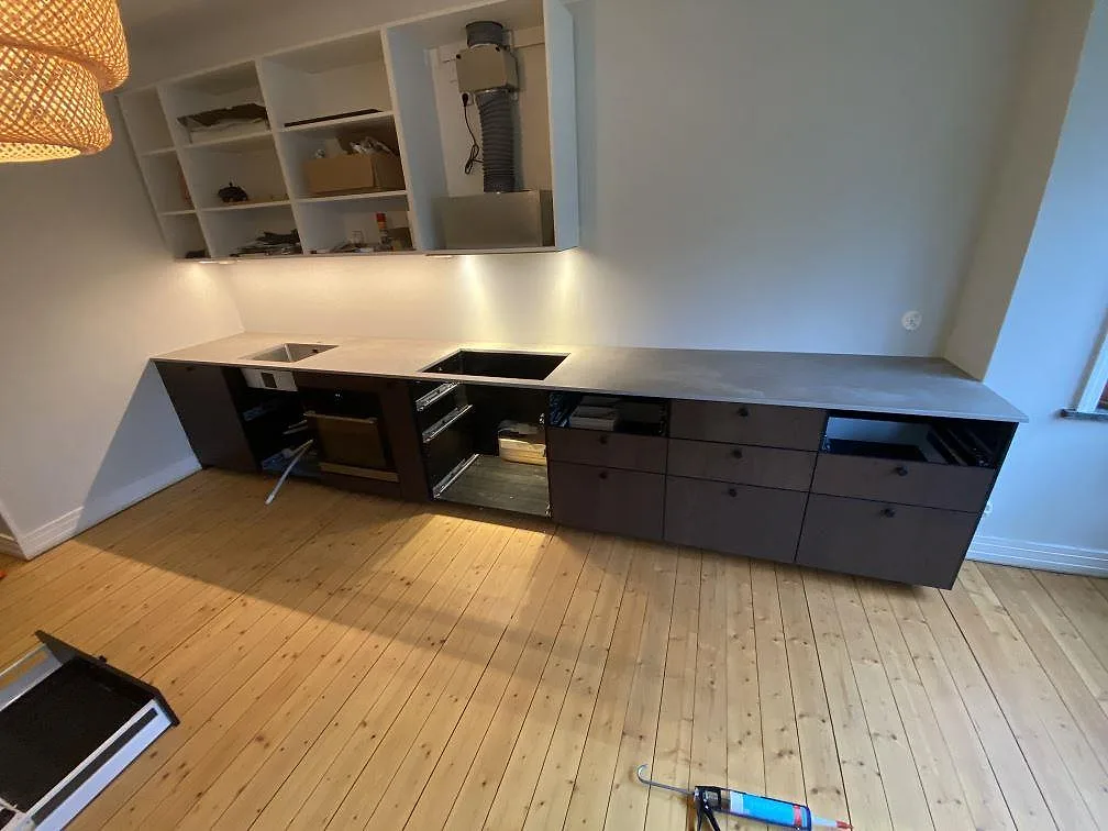 Køkkenbordplade i grå Dekton Keon med mat betonglook, lang sammanhängande bordplade med udskæring for vask og kogeplade i ett køkken under montering i Malmö.