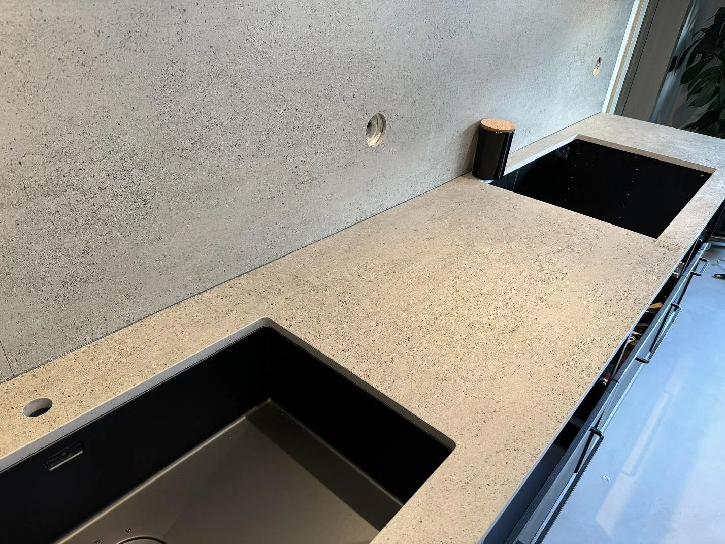 Køkkenbordplade i mat Dekton Keon med matchande stænkplade og sort vask i ett køkken i Malmö.