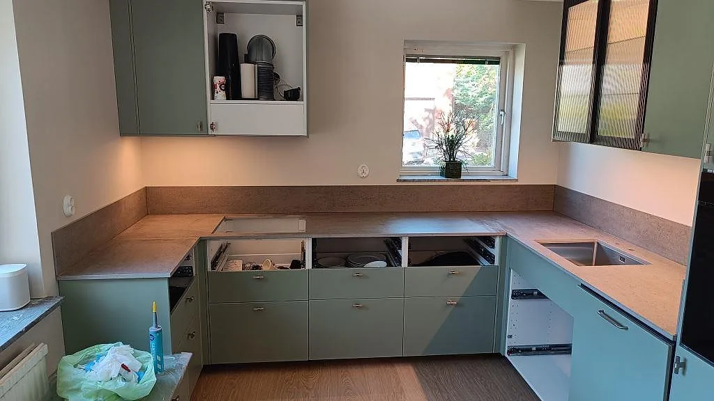 Køkkenbordplade i mat grå Dekton Keon, keramik, med stænkplade og synlig rostfri vask under montering i ett køkken i Sävedalen.