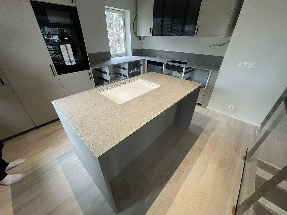 Køkkenbordplade i ljusgrå Dekton Keon, mat keramik, med køkkenø, diskplats og kogeplade i ett køkken i Västerås.